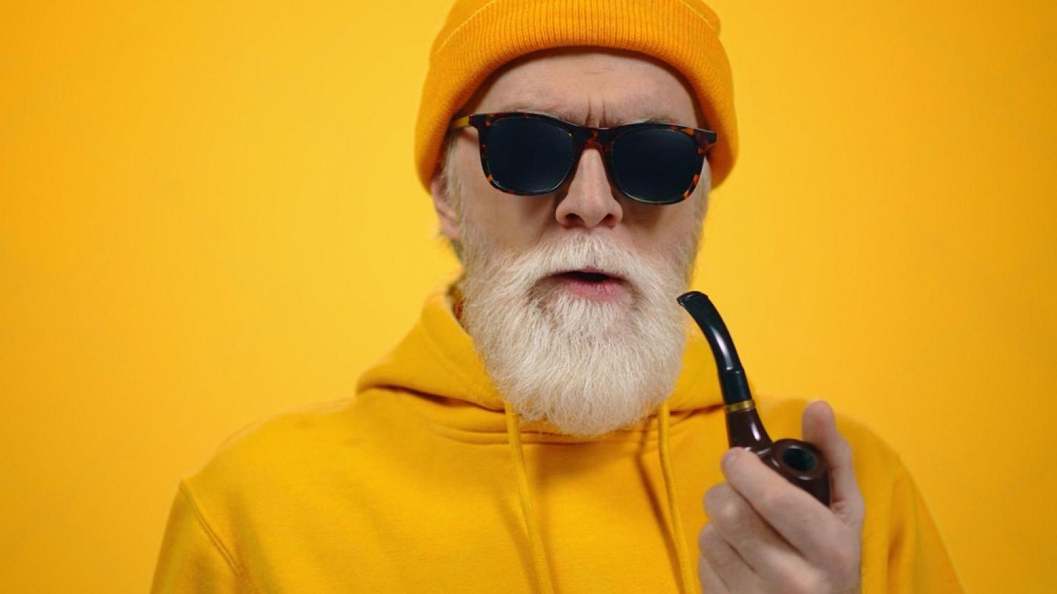 Older man in a yellow hoodie holding a smoking pipe, illustrating long-term smoking habits